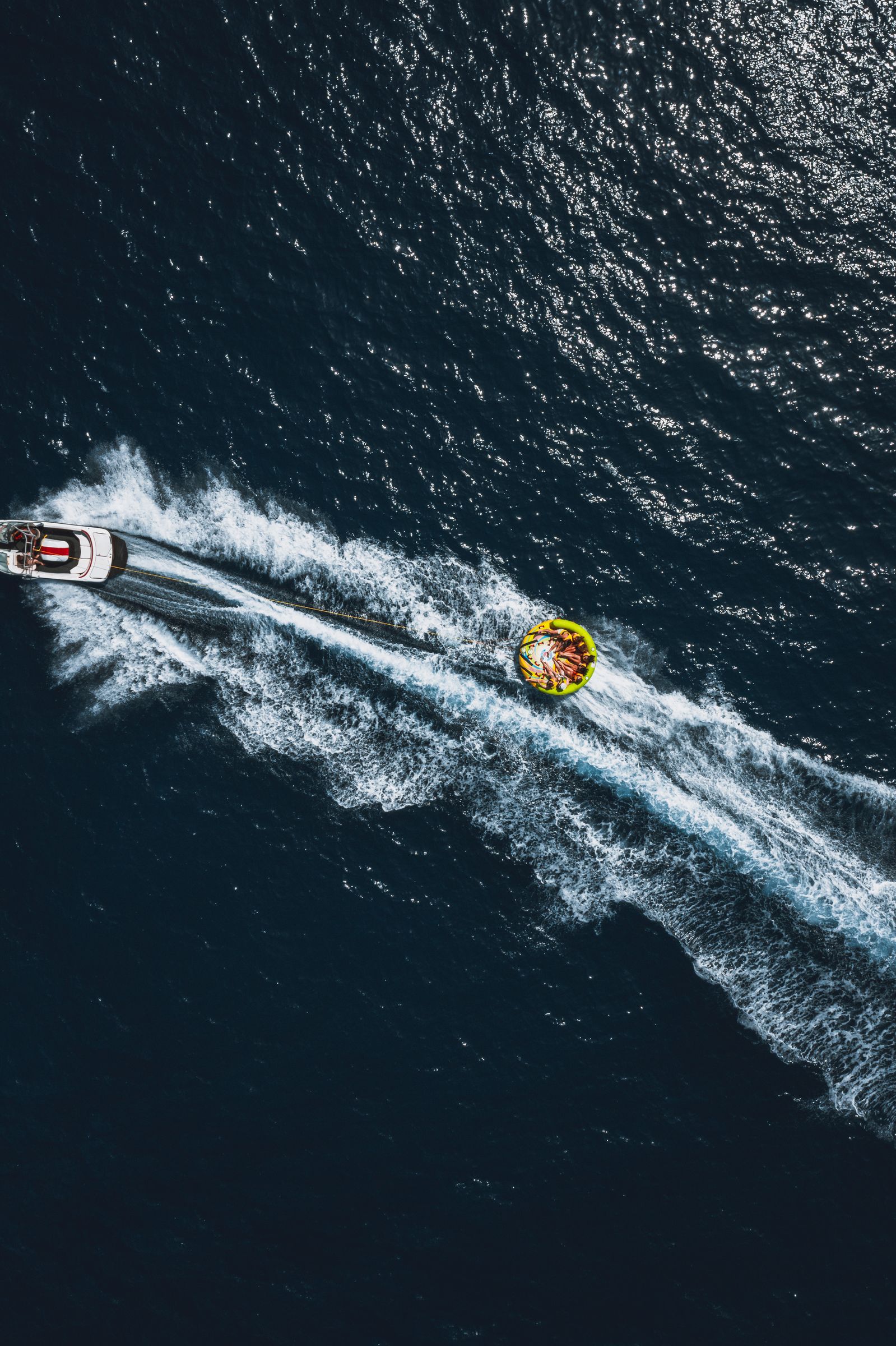A speedboat towing a ring across deep water, wake trails cutting the frame.