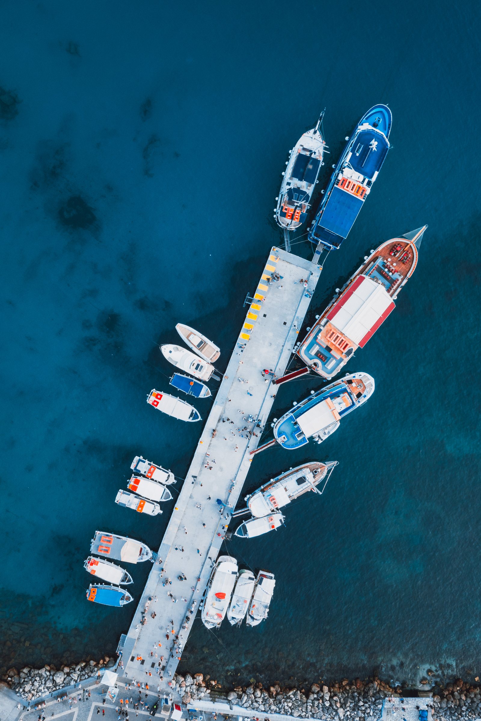 Boats moored either side of a pier, seen straight down.