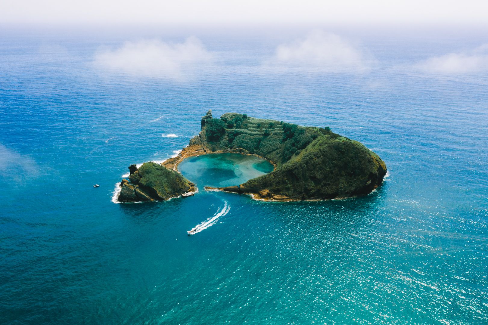 A ringed green islet from above, a boat passing, Azores.