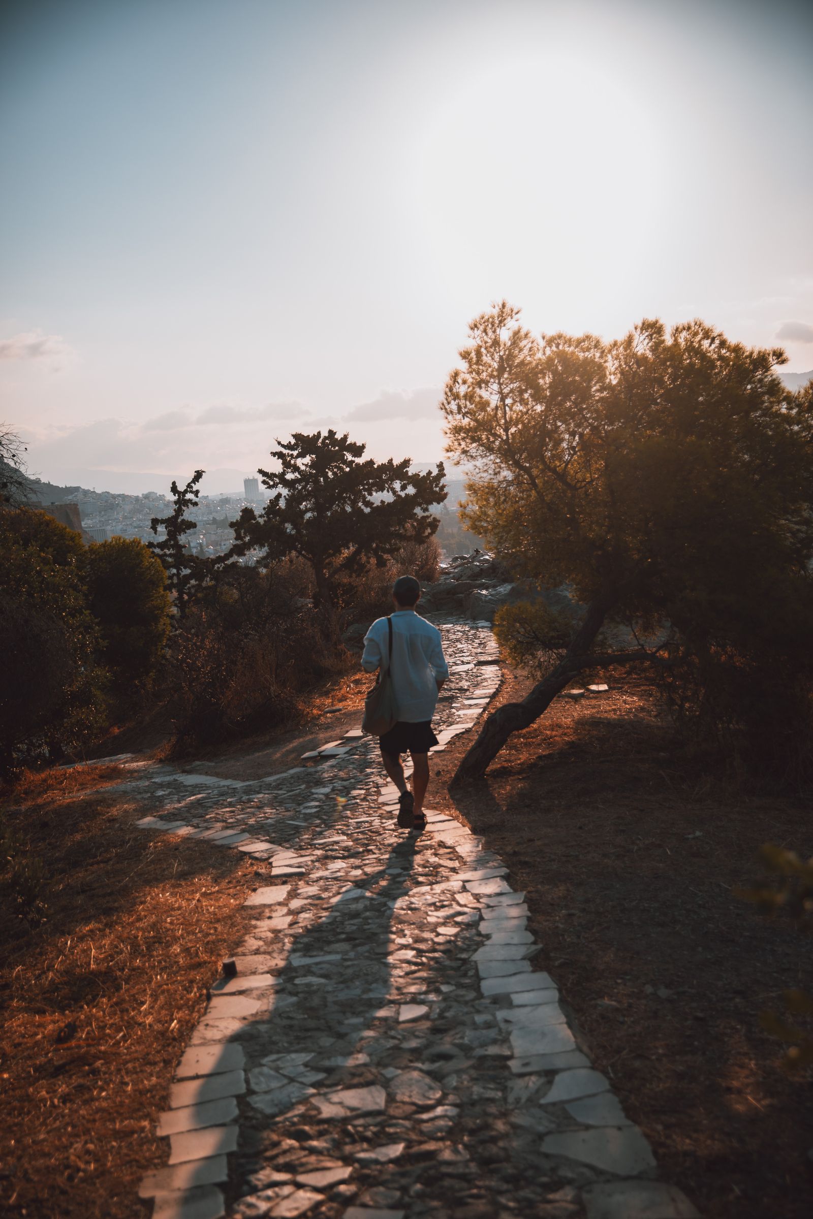 A backlit stone path below the Acropolis, a lone walker heading into golden light.