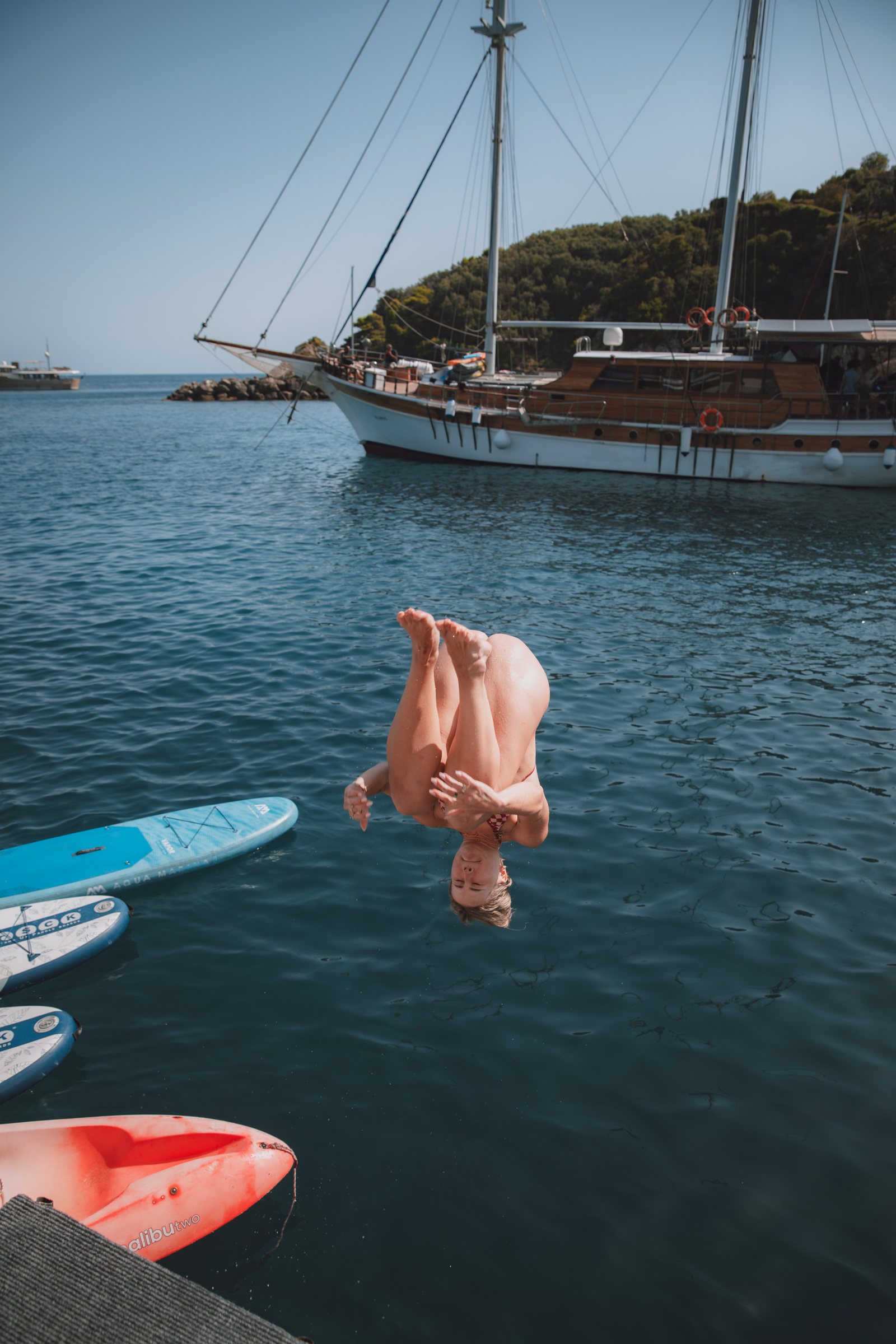 Diving from the deck of the gulet, paddleboards scattered on the water below.
