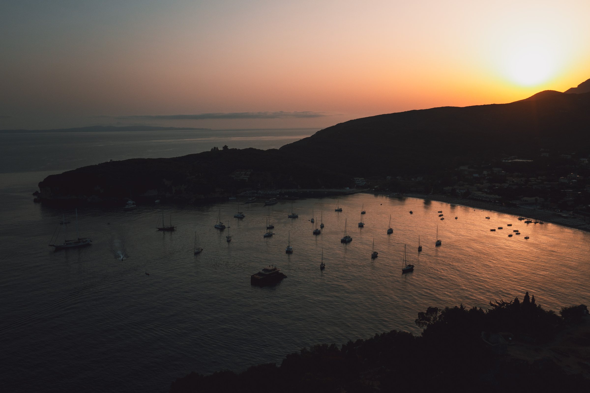 The sun going down behind the headland, boats anchored in silhouette.